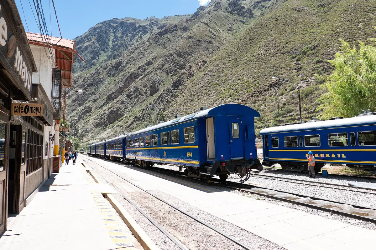 Blue train carriages standing at a platform in Ollantaytambo station, with a steep dry mountainside rising behind